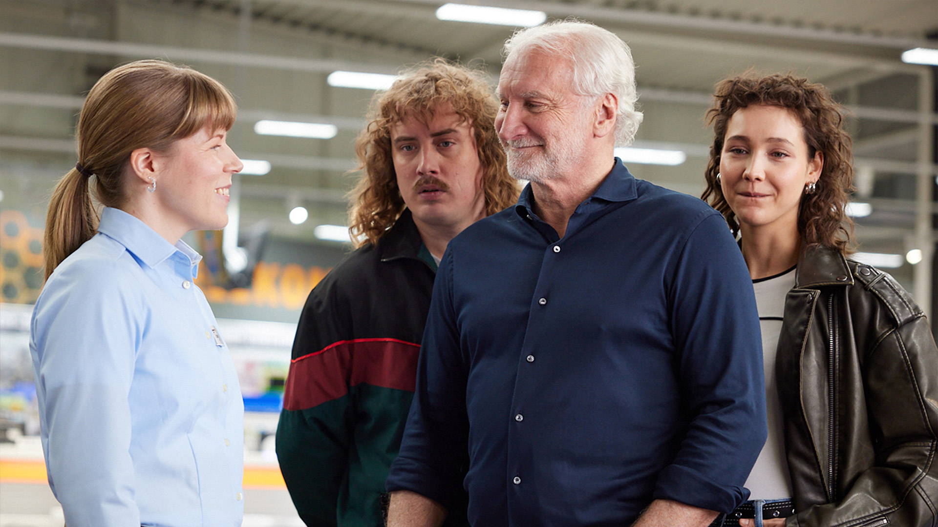 Rudi Völler steht lächelnd mit einem Mann und einer Frau hinter sich vor einer Expert-Verkäuferin.