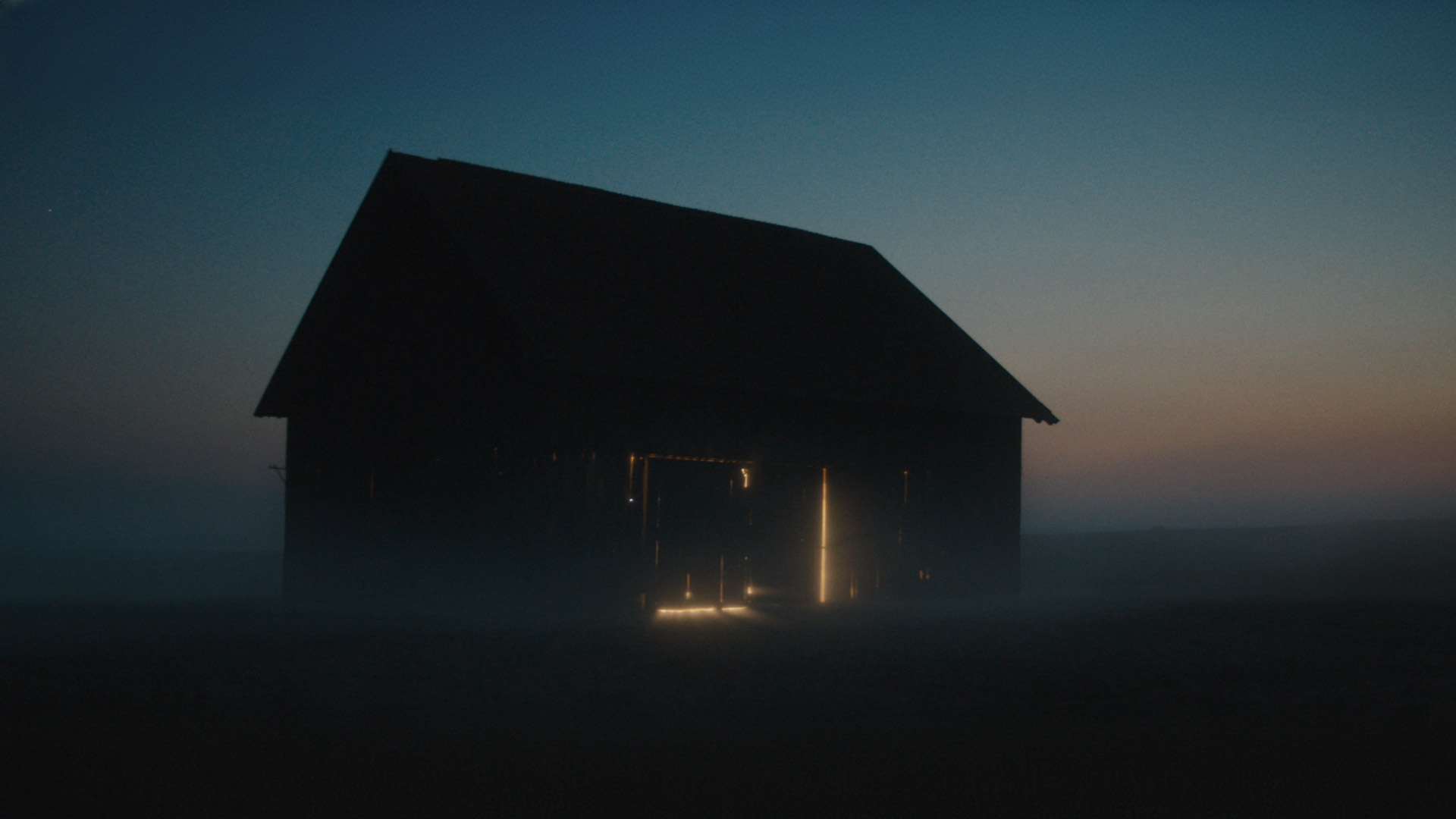 Ein Scheune in der späten Abenddämmerung. Aus ihr leuchten helle Lichter.