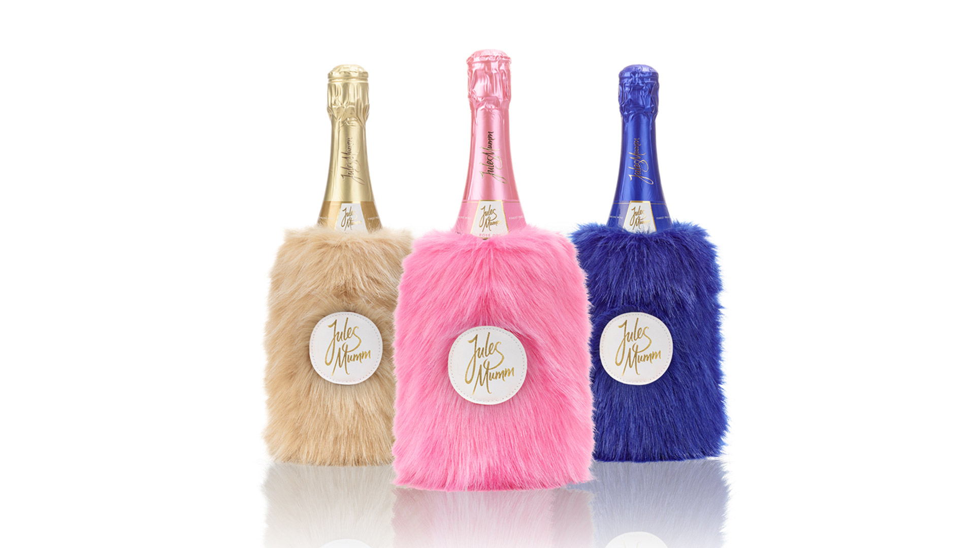 Eine goldene, eine pinke und eine blaue Flasche Jules Mumm. Jeweils in einem flauschigen Felltäschchen.